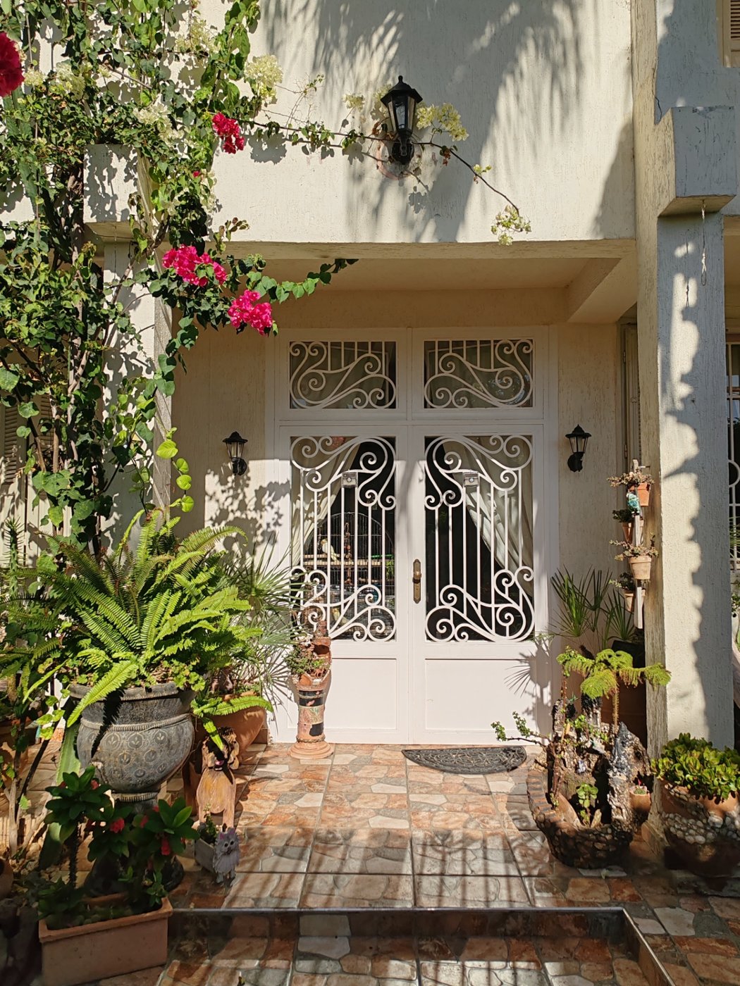 Main entrance — wrought-iron double doors framed by bougainvillea
